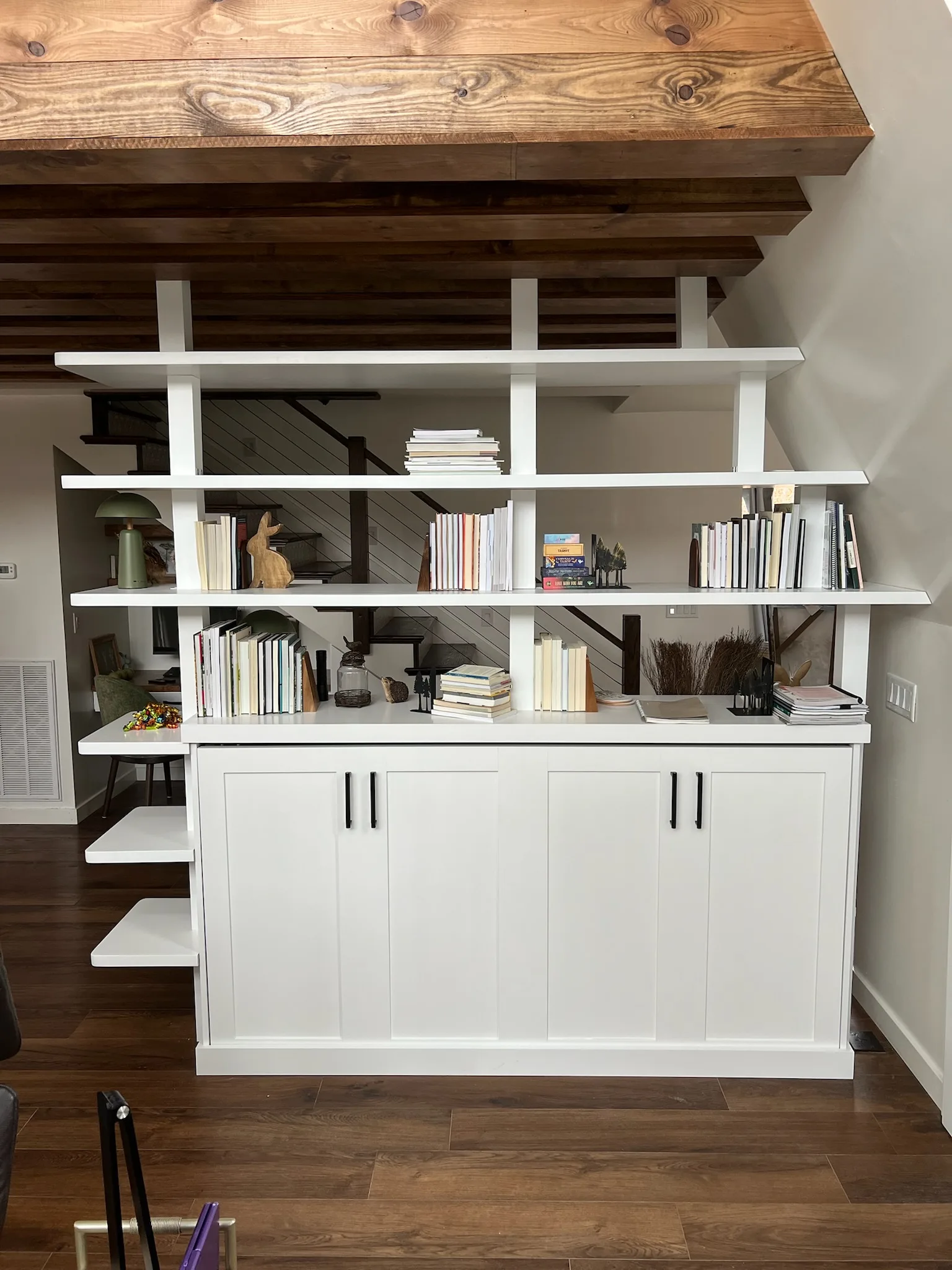 Wide front view of white bookshelf room divider with staircase and exposed beams by Sims Custom Woodwork.