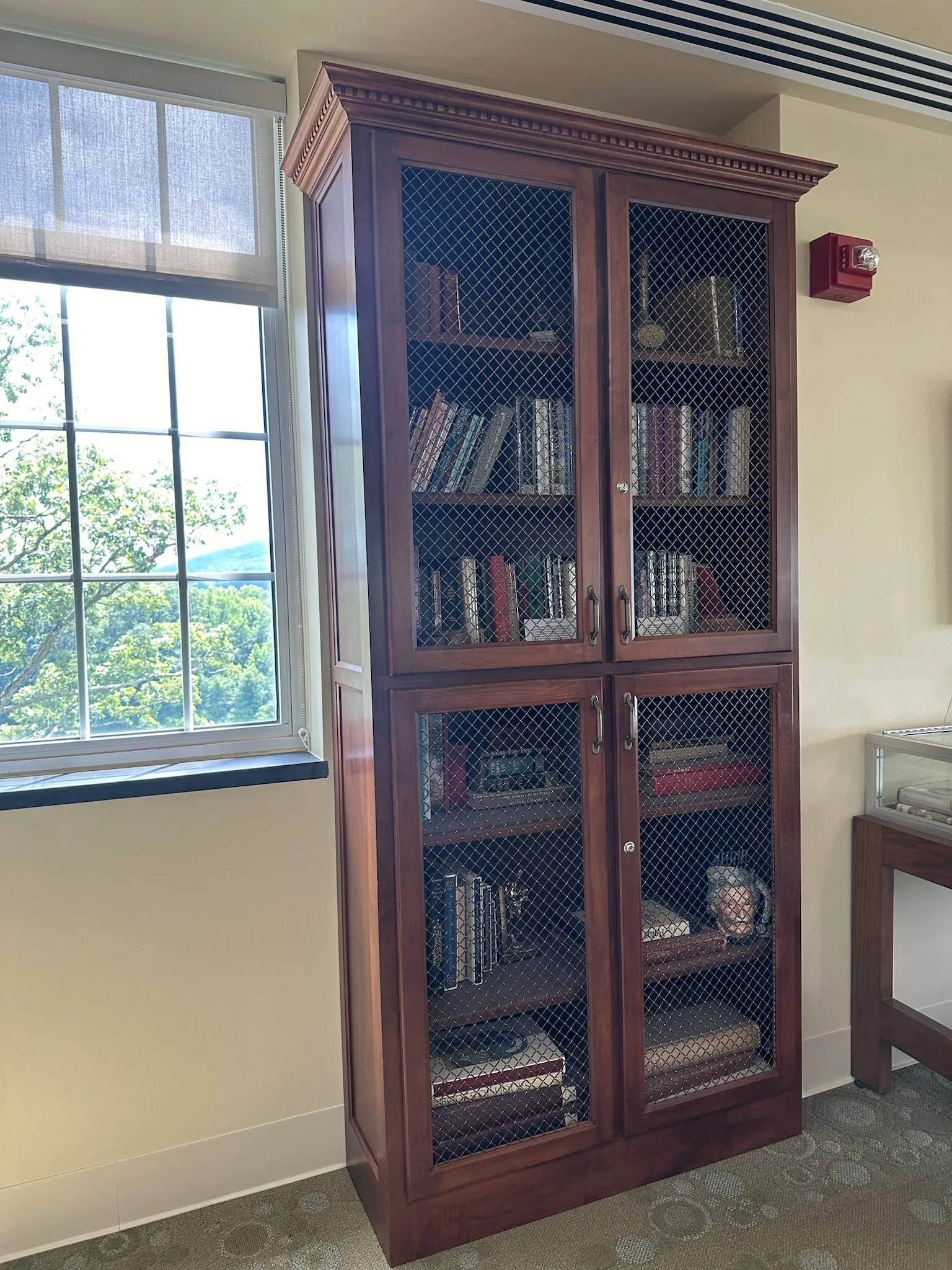 Cherry stained bookcase with wire mesh doors and crown molding by Sims Custom Woodwork.