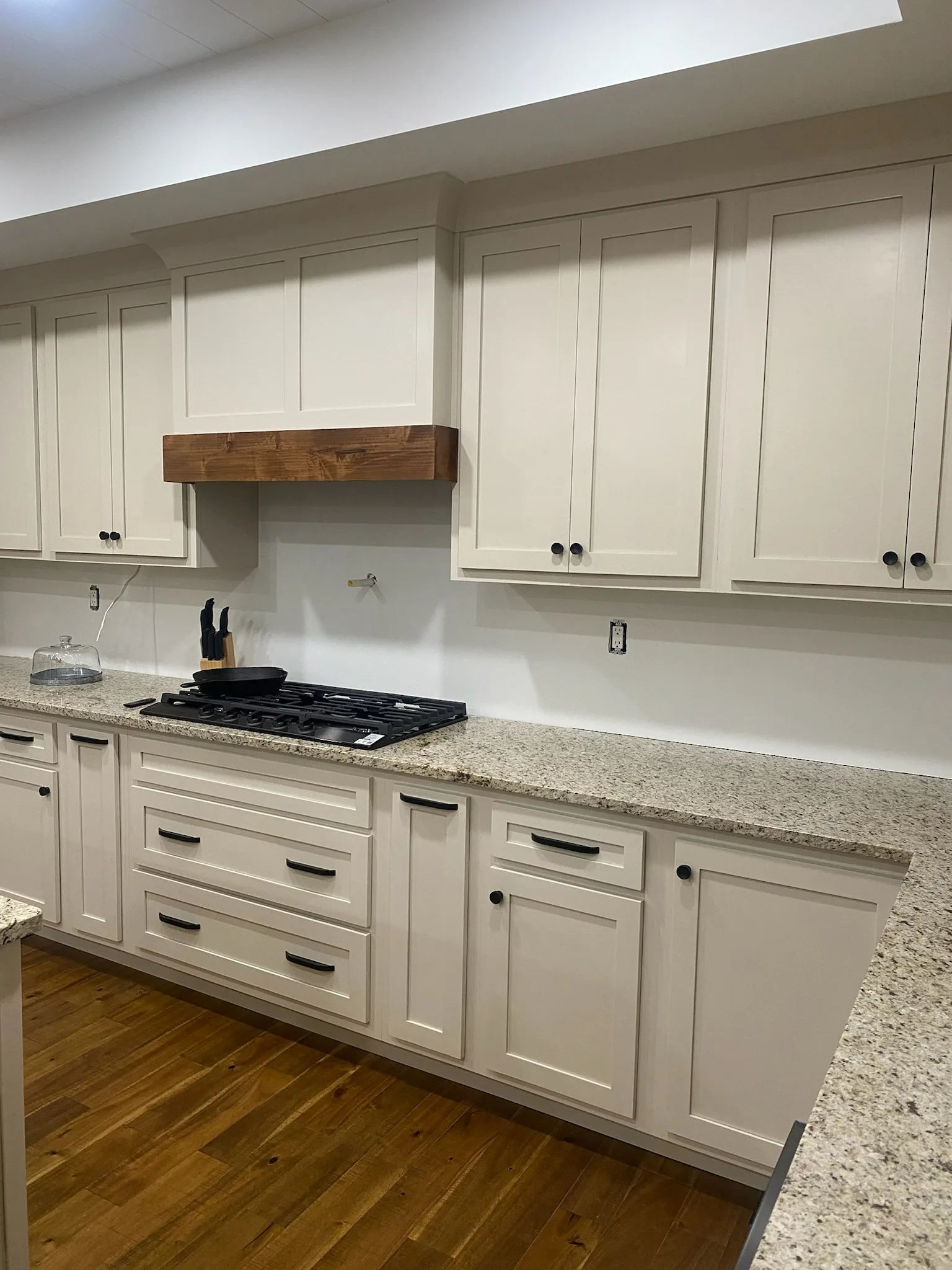 Cream shaker kitchen cooktop wall with walnut range hood and granite counters by Sims Custom Woodwork.