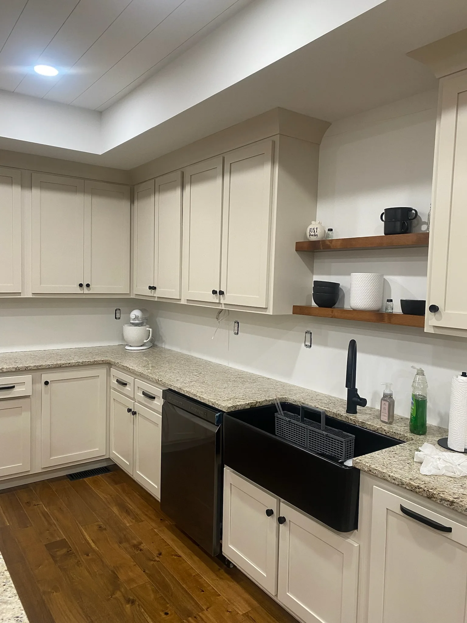 Cream shaker kitchen with black farmhouse sink and walnut floating shelves by Sims Custom Woodwork.