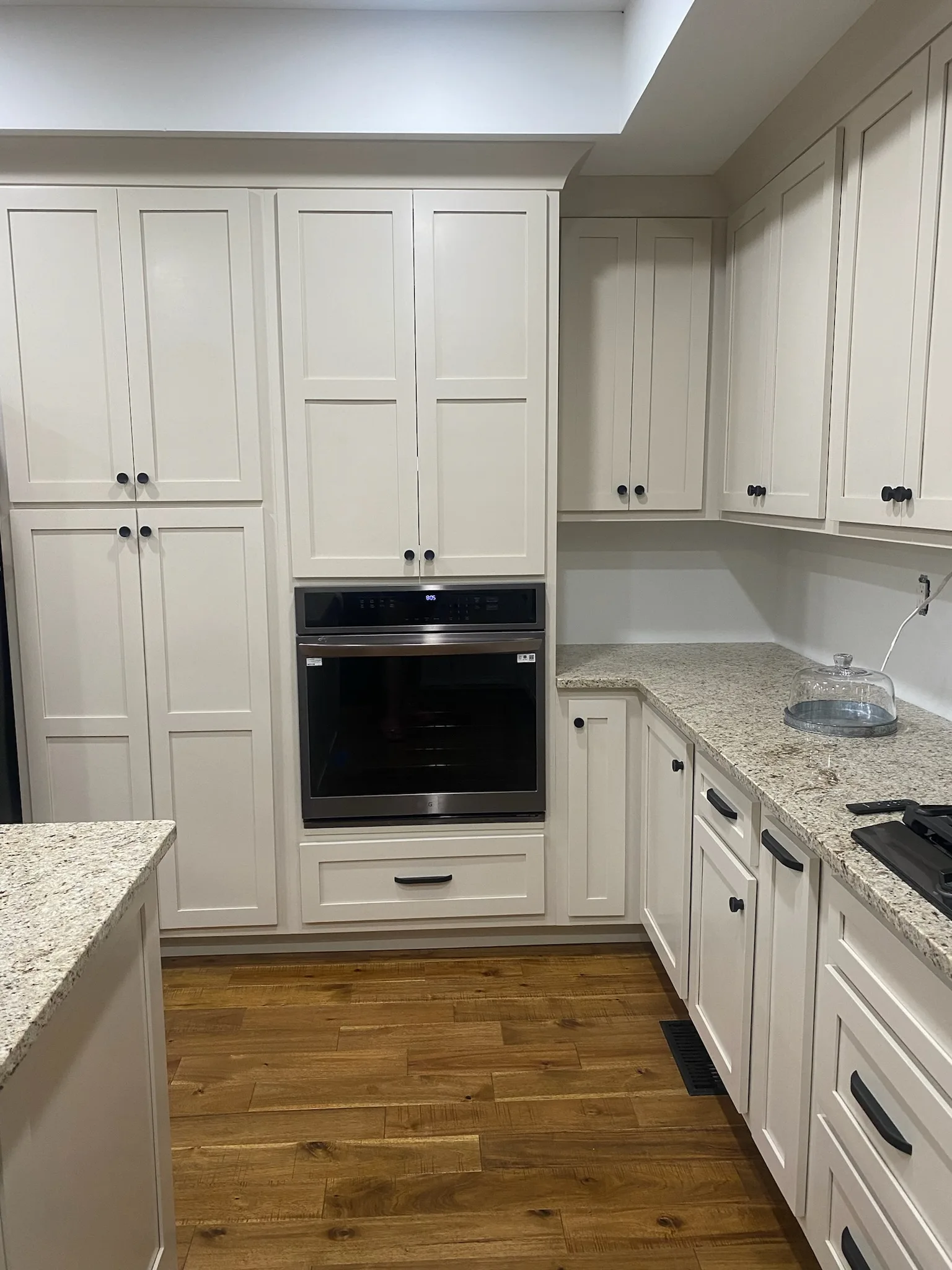 Cream shaker kitchen oven and pantry wall with granite countertops by Sims Custom Woodwork.