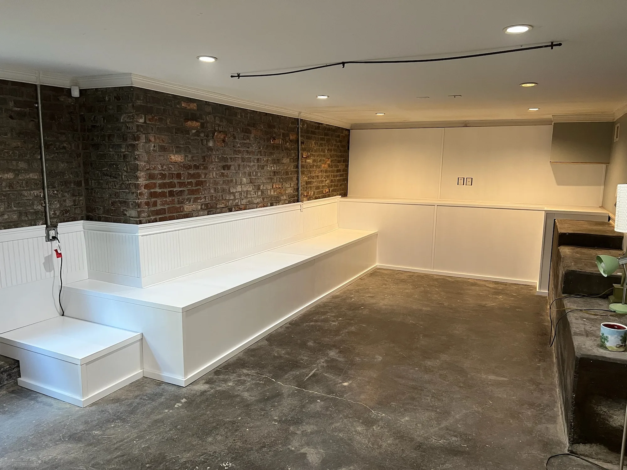 Custom tiered built-in seating with beadboard panels against exposed brick wall by Sims Custom Woodwork.