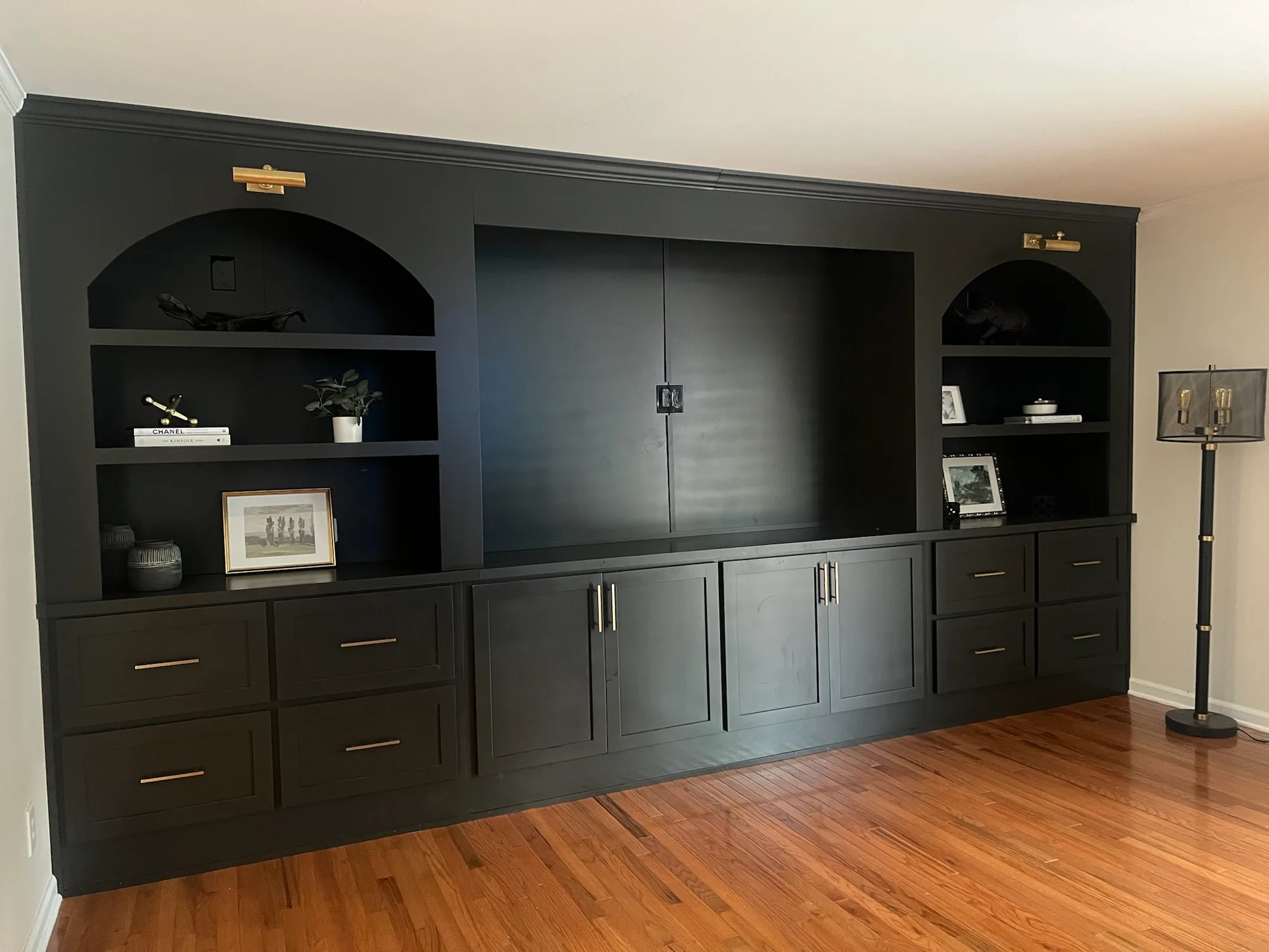 Dark built-in entertainment center with arched niches and brass hardware by Sims Custom Woodwork.