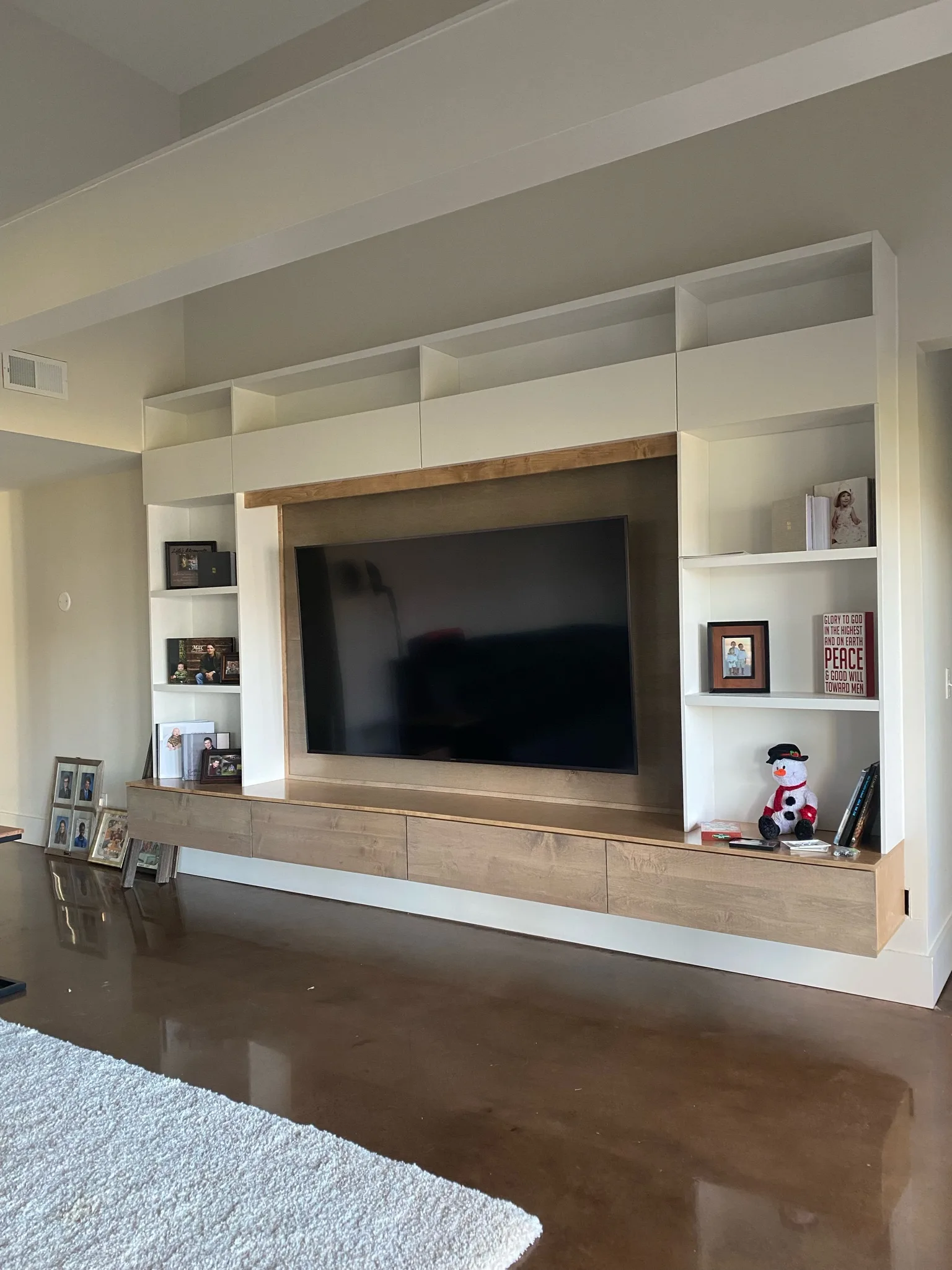 Custom floor-to-ceiling entertainment center with wood accents and open shelving by Sims Custom Woodwork.