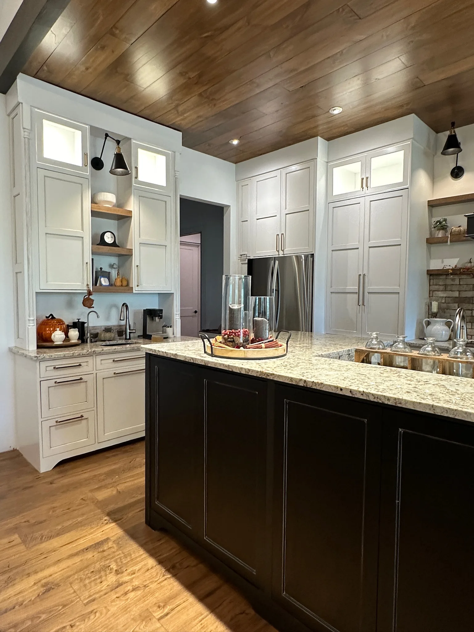 Wide-angle overview of farmhouse kitchen with dark island and white cabinets by Sims Custom Woodwork.