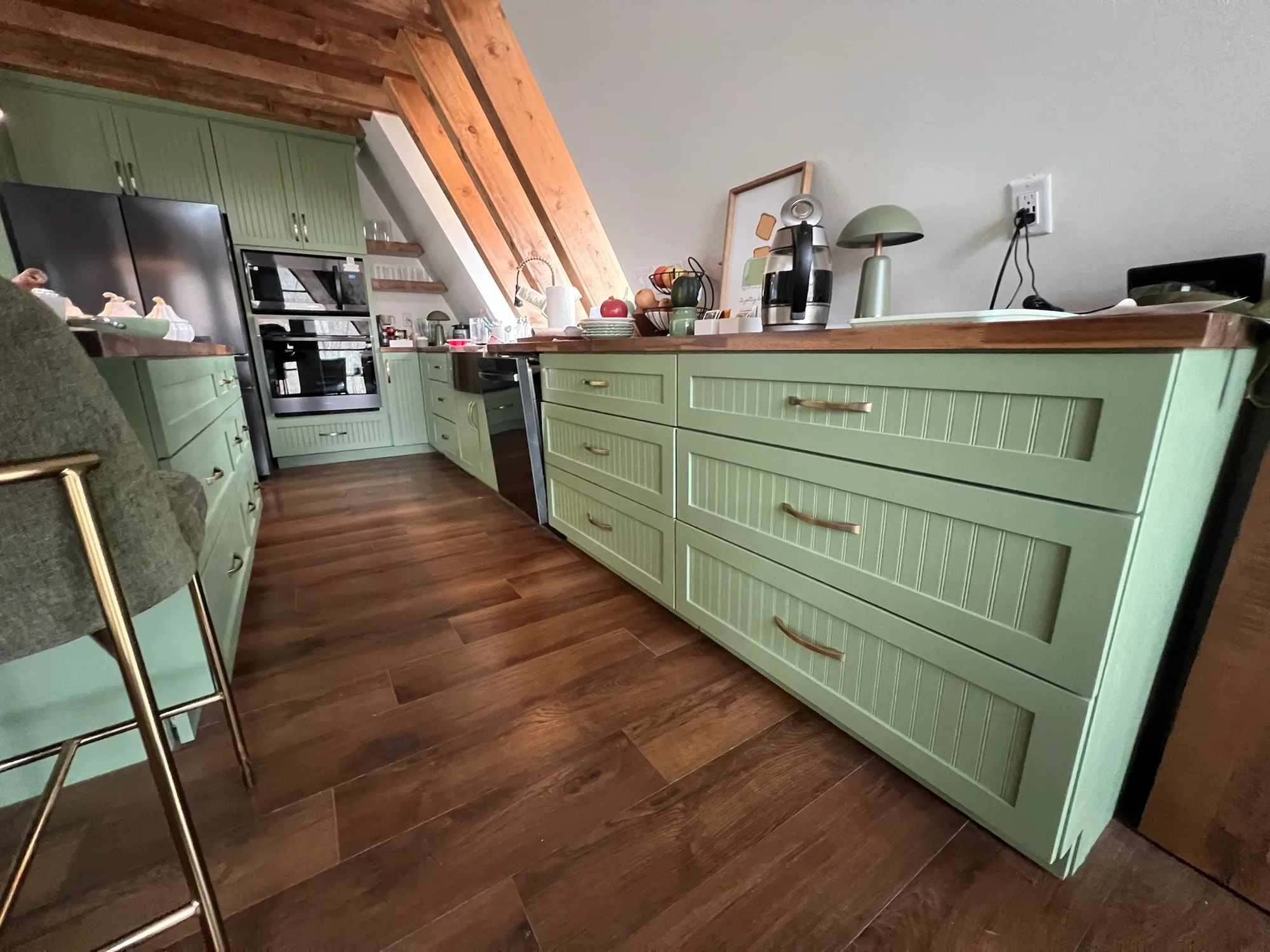 Sage green beadboard island drawers with walnut countertops and brass hardware by Sims Custom Woodwork.