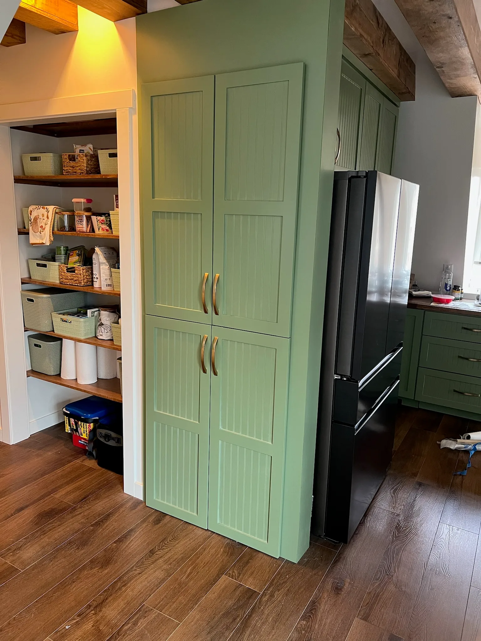 Sage green beadboard pantry tower with brass handles and fridge surround by Sims Custom Woodwork — Chattanooga area custom kitchen cabinetry.