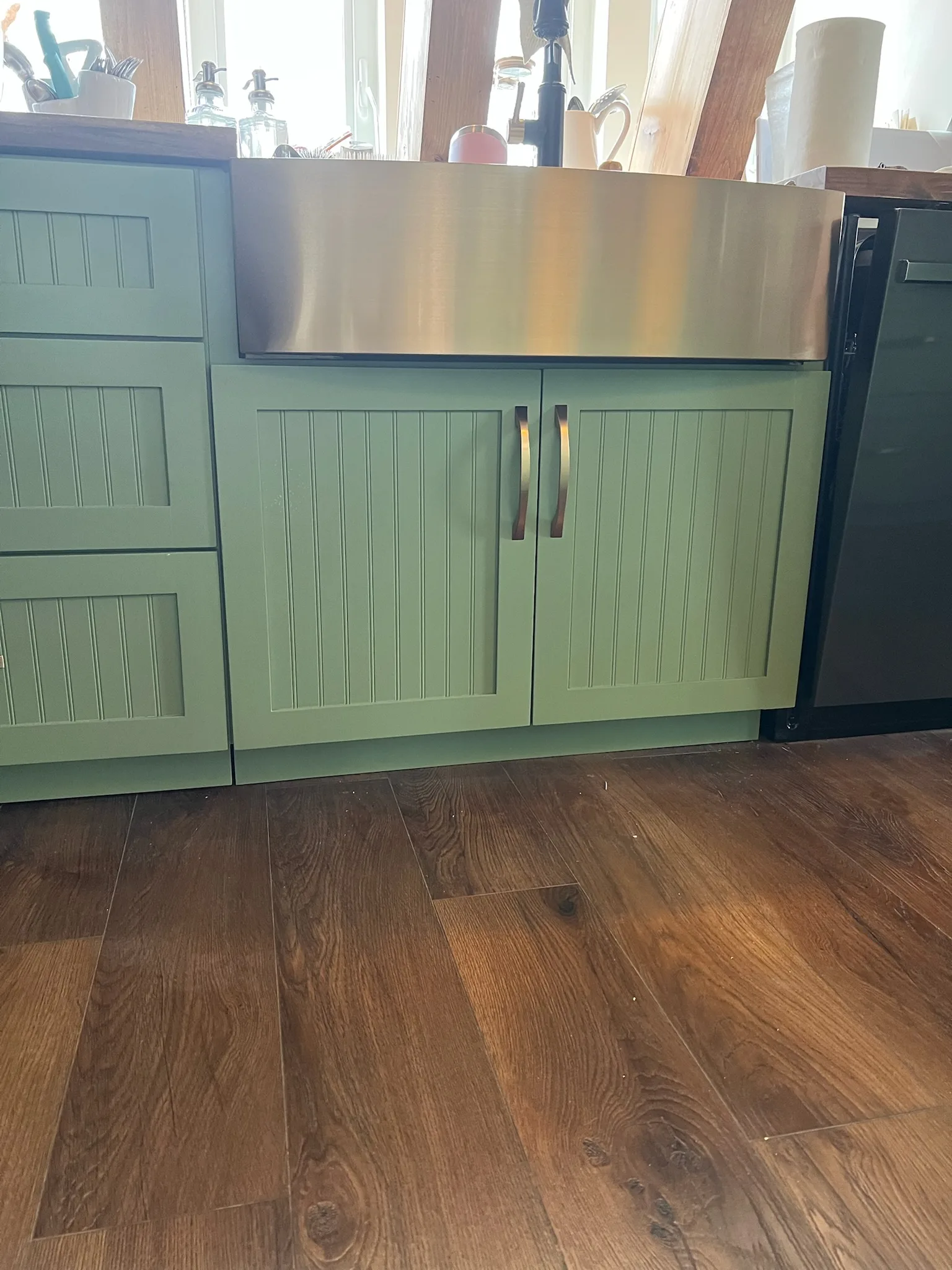 Green beadboard sink base with farmhouse sink and brass pulls by Sims Custom Woodwork.