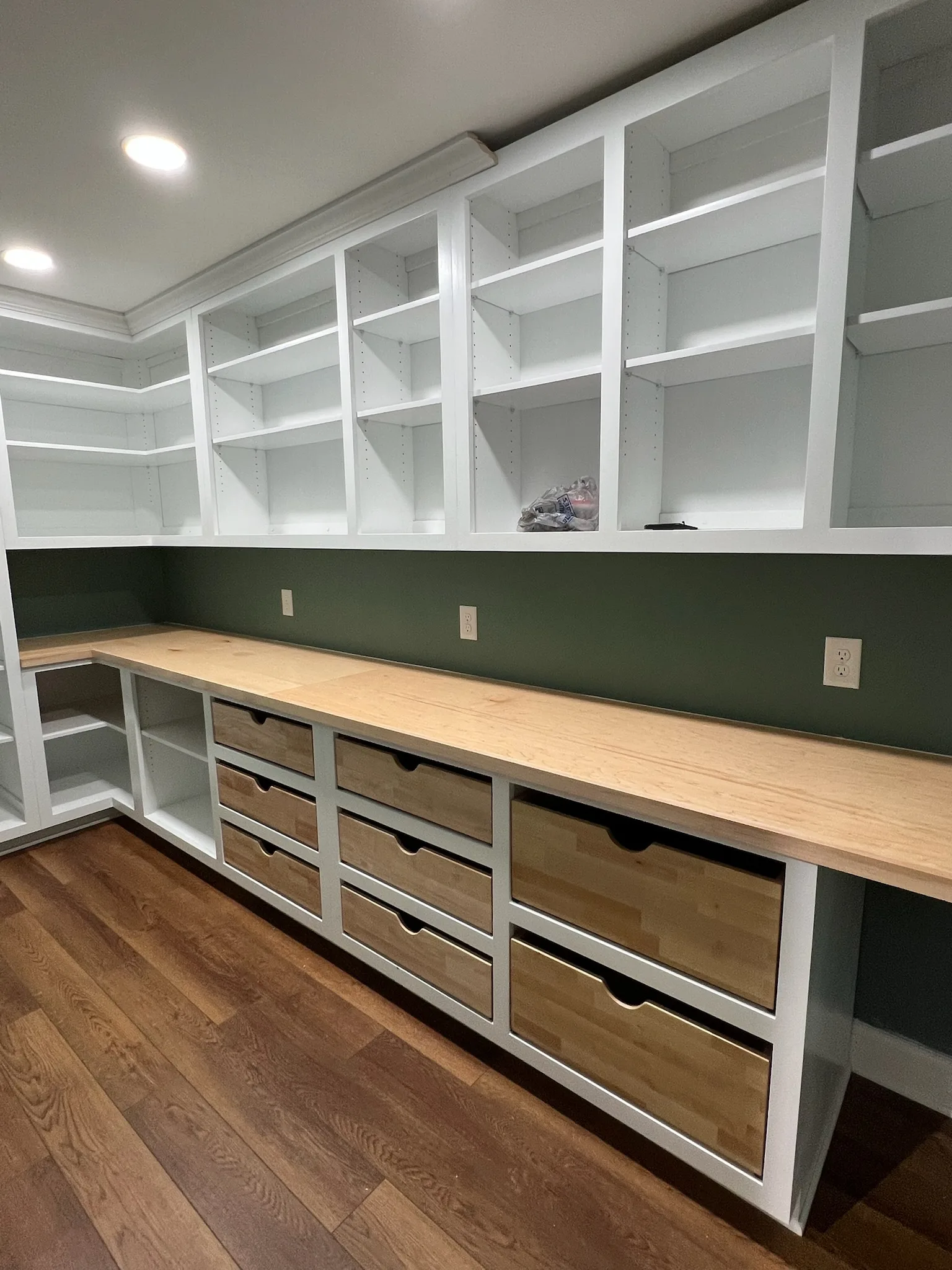 Walk-in pantry with dark green walls, white shelving, and natural wood drawers by Sims Custom Woodwork.