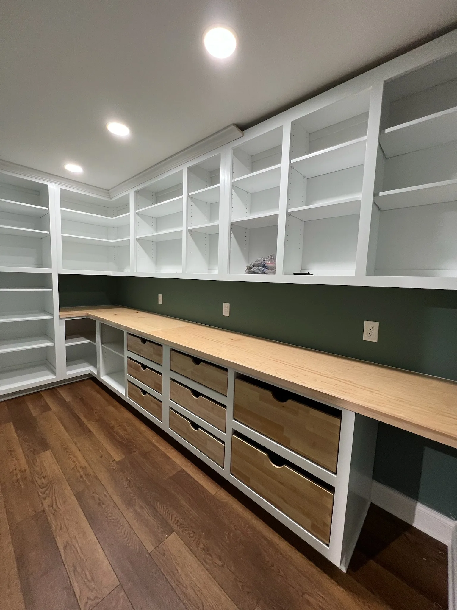 Wide-angle view of L-shaped walk-in pantry with green walls and wood drawers by Sims Custom Woodwork.