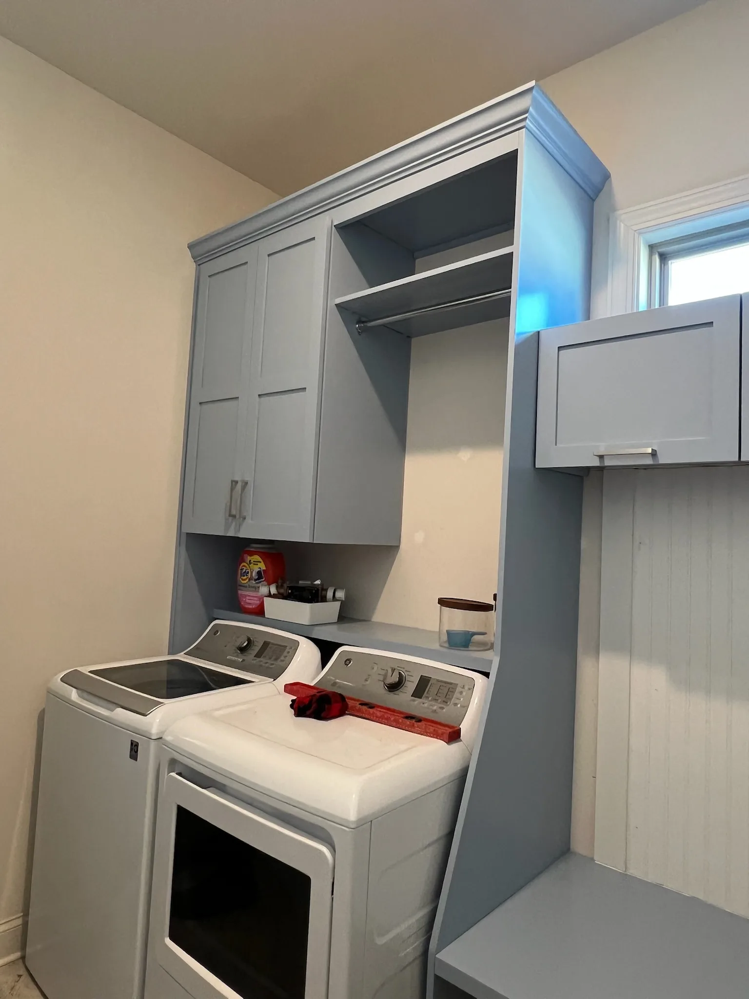 Custom blue-grey laundry room cabinetry with washer surround and hanging rod by Sims Custom Woodwork.