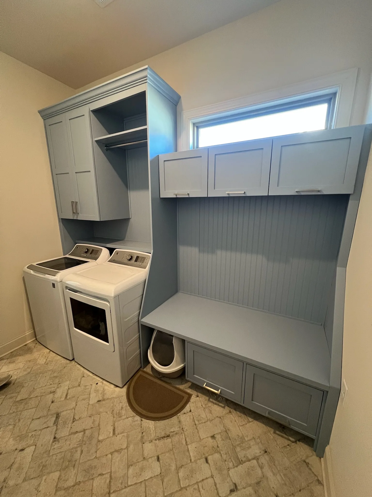 Wide-angle view of blue-grey laundry room with washer surround and folding station by Sims Custom Woodwork.