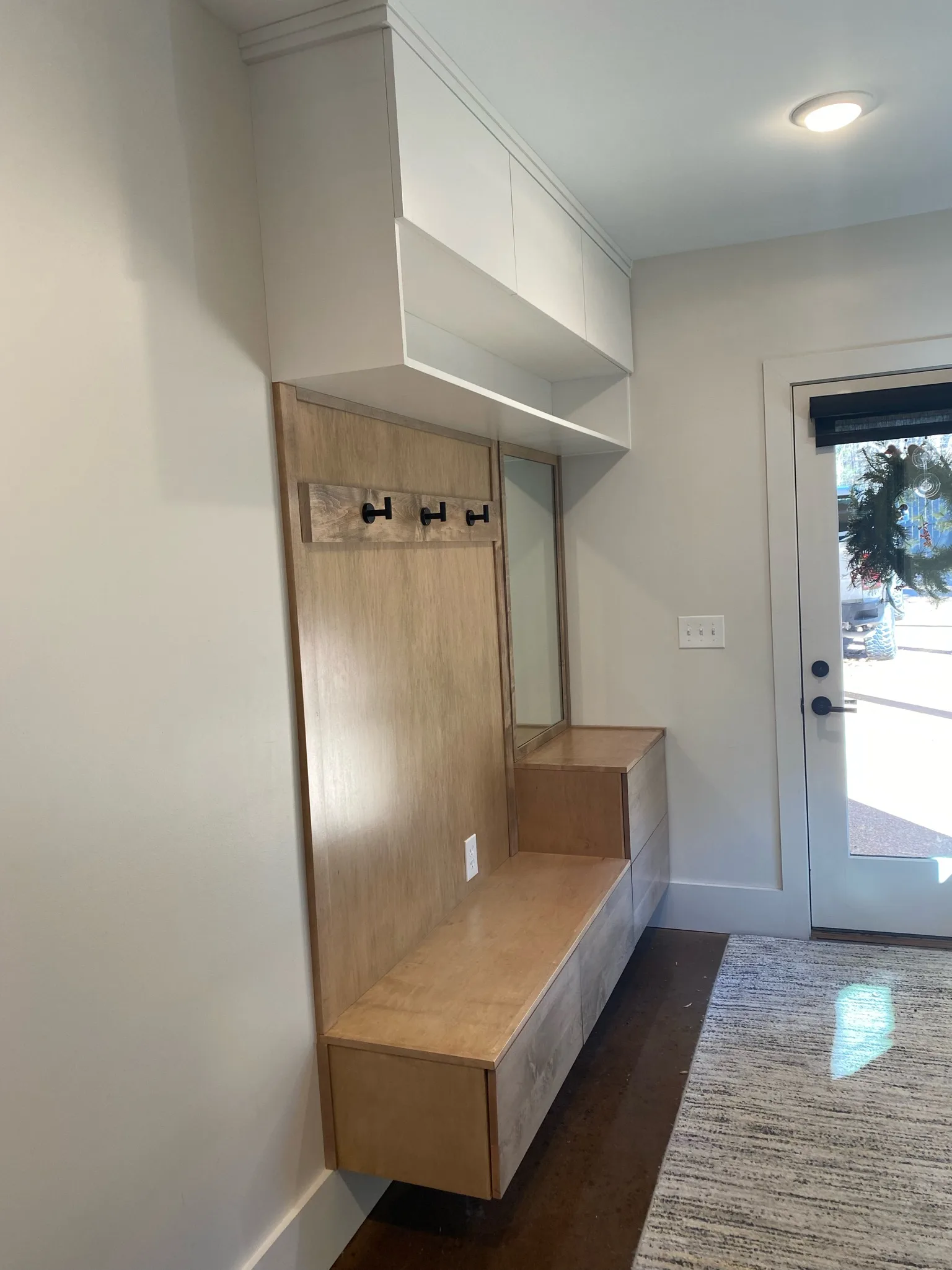 Custom mudroom bench with coat hooks and upper cabinets by Sims Custom Woodwork.
