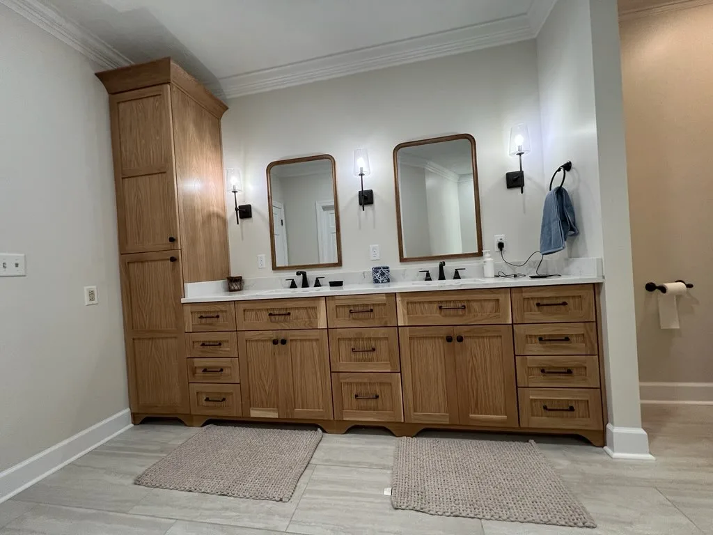 Angled view of natural wood double vanity with linen tower and dual mirrors by Sims Custom Woodwork.