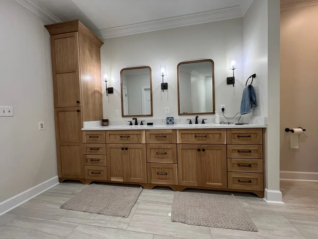 Natural wood double bathroom vanity with linen tower, white stone countertop, and matte black fixtures by Sims Custom Woodwork.