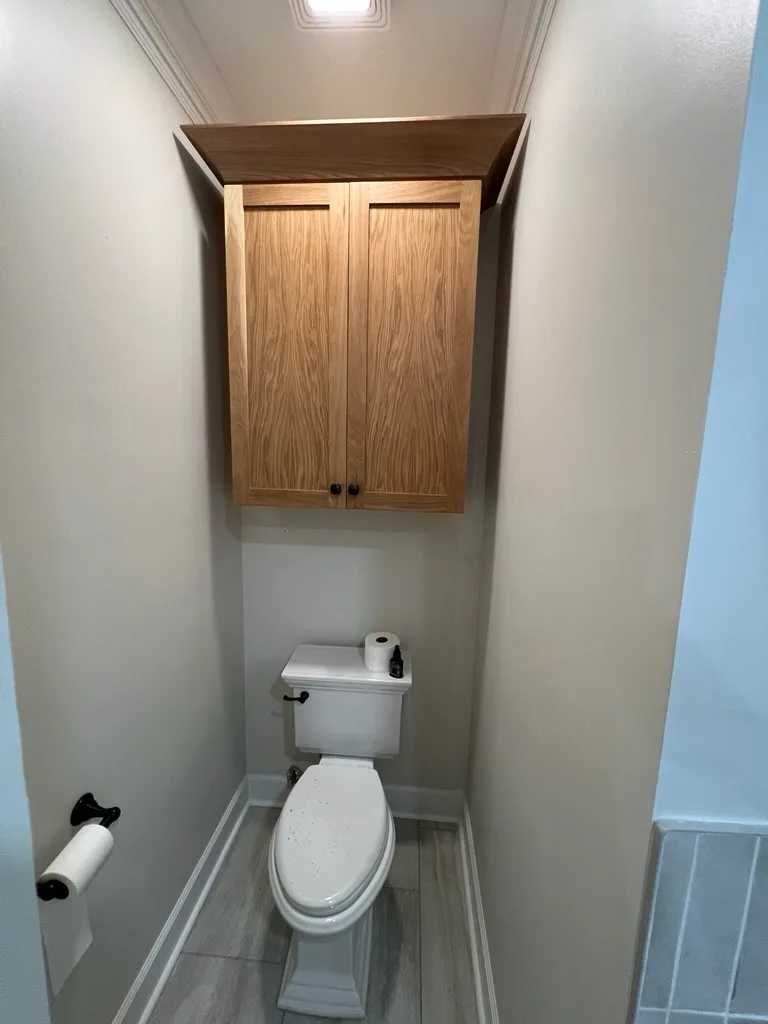 Matching natural wood over-toilet bathroom cabinet with black knobs by Sims Custom Woodwork.