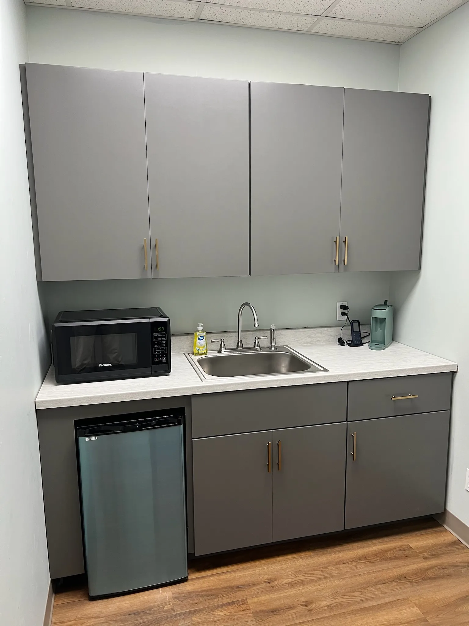 Dental office staff kitchenette with gray flat-panel cabinets and brushed gold hardware by Sims Custom Woodwork.