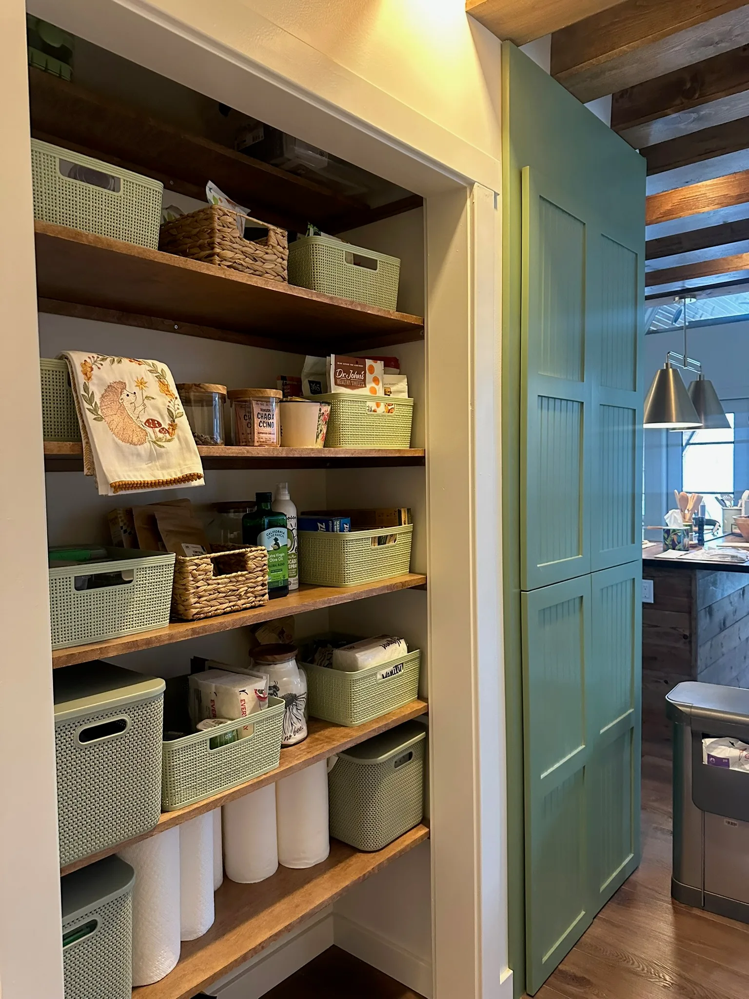 Rustic pantry with natural wood shelves and sage green beadboard door by Sims Custom Woodwork.