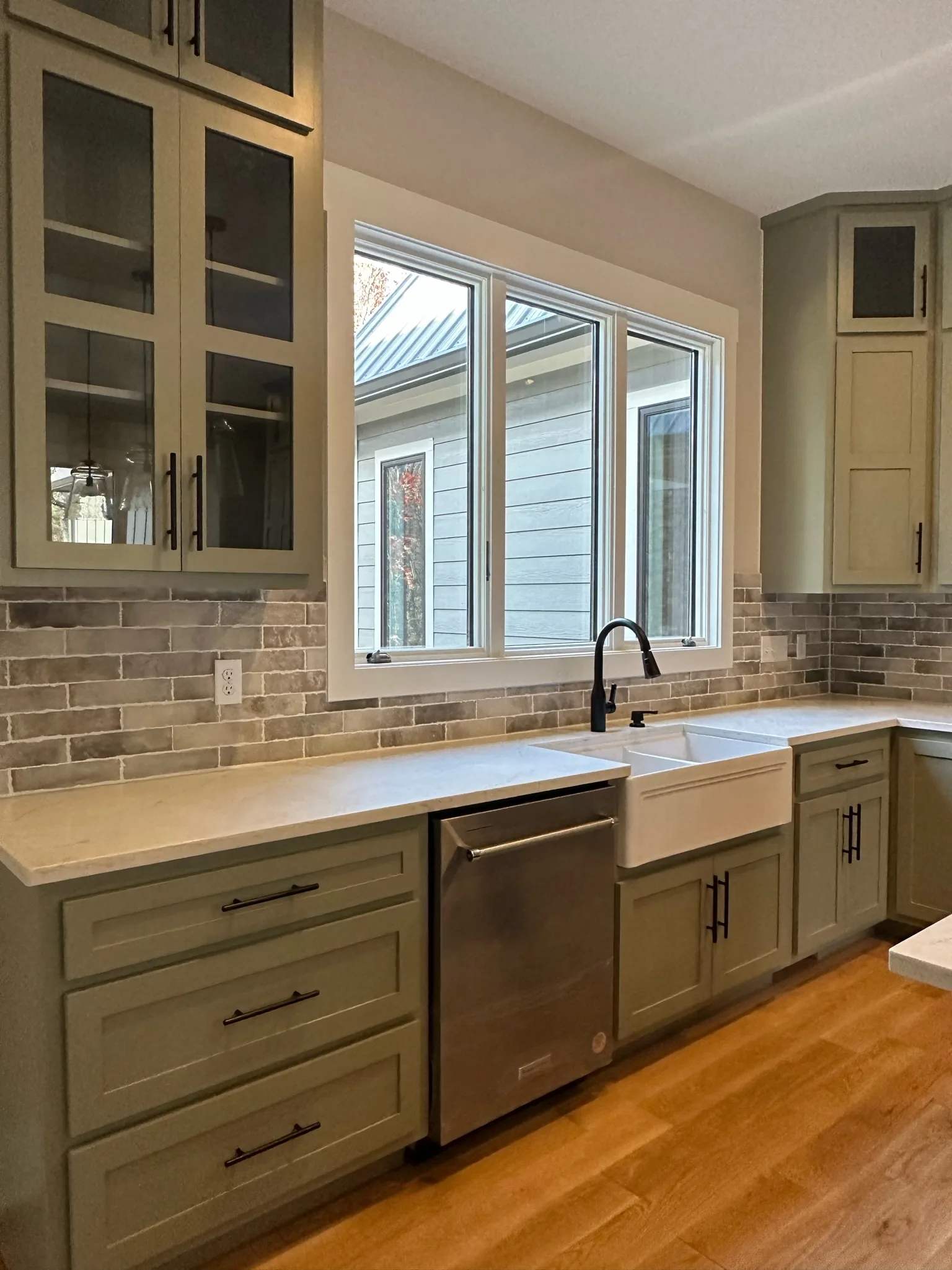 Wide view of sage green kitchen sink wall with farmhouse sink and stone backsplash by Sims Custom Woodwork.