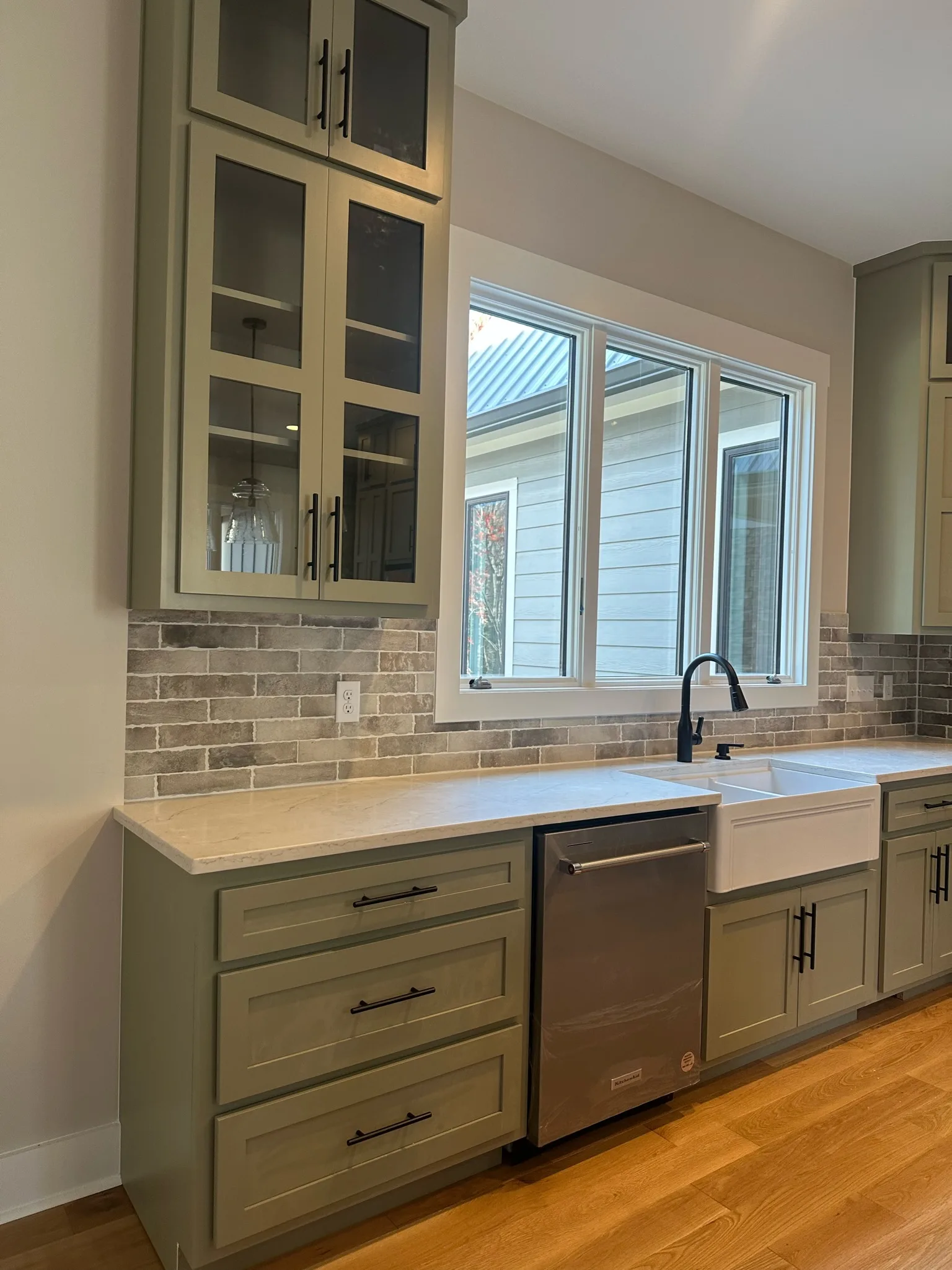 Sage green shaker kitchen sink wall with farmhouse sink and stone backsplash by Sims Custom Woodwork.