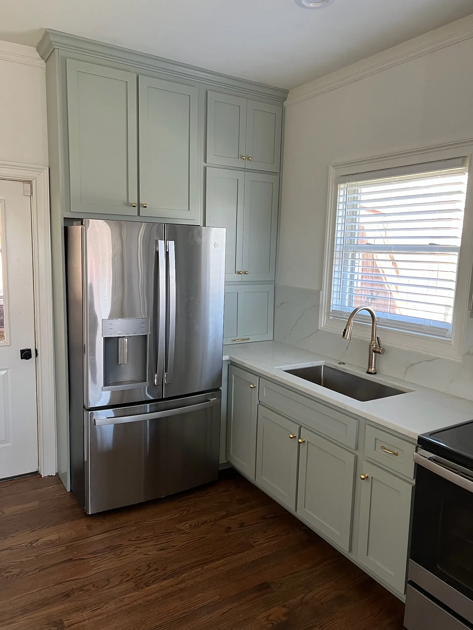 Sage green pantry cabinets flanking stainless refrigerator with gold faucet by Sims Custom Woodwork.