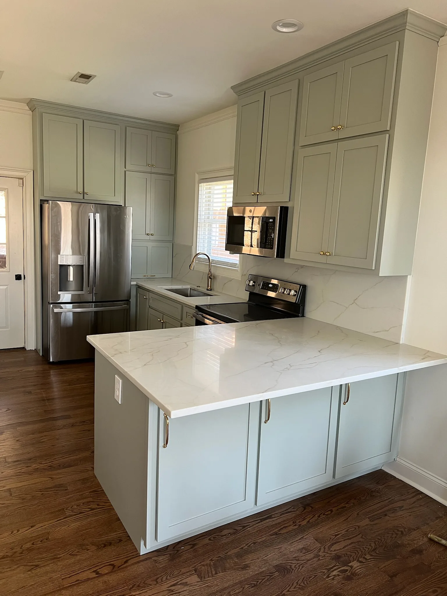 Sage green shaker kitchen with quartz island and brass hardware by Sims Custom Woodwork — serving Chattanooga, TN and North Georgia.