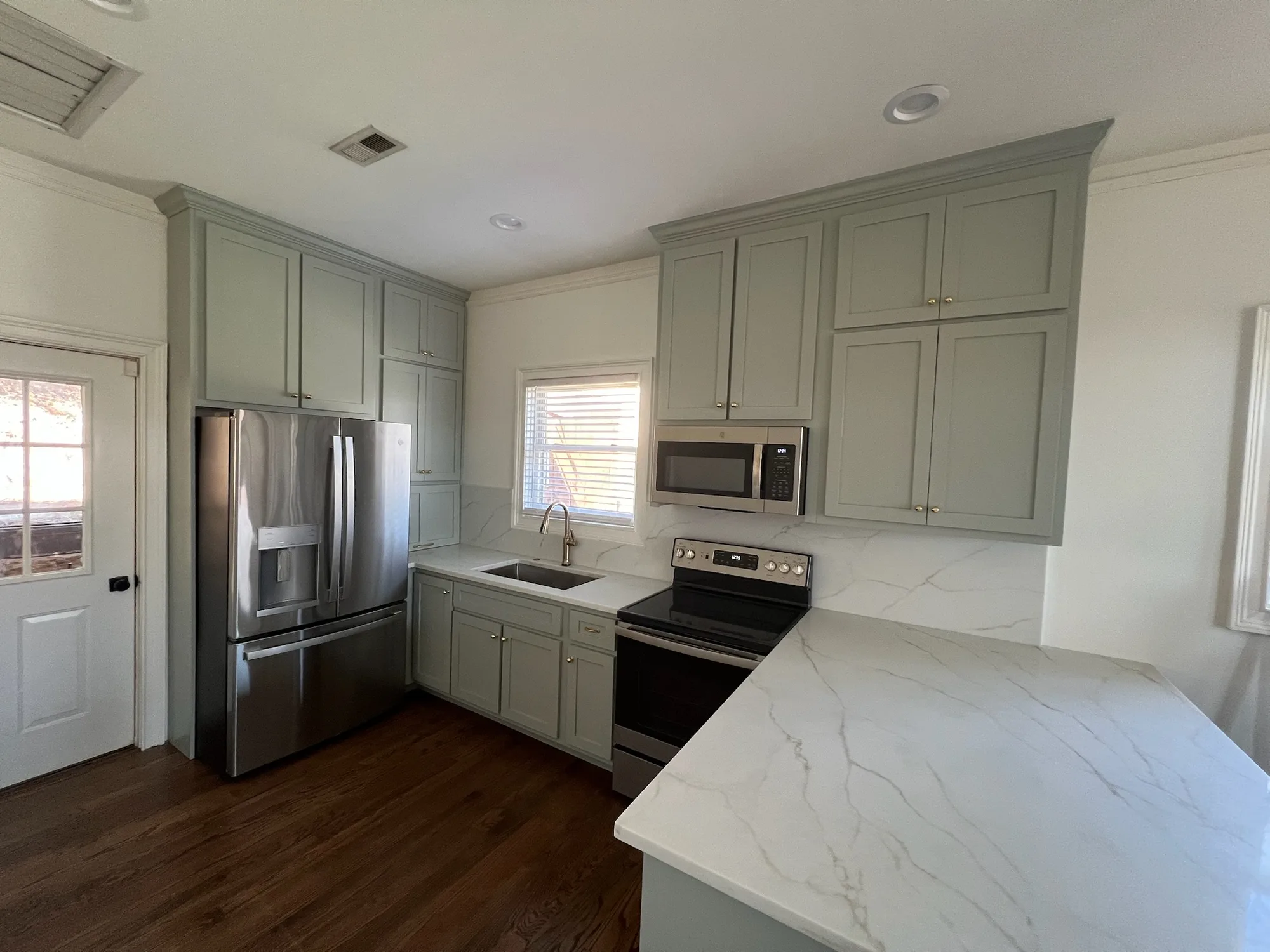 Full perimeter view of sage green shaker kitchen with quartz countertops by Sims Custom Woodwork.