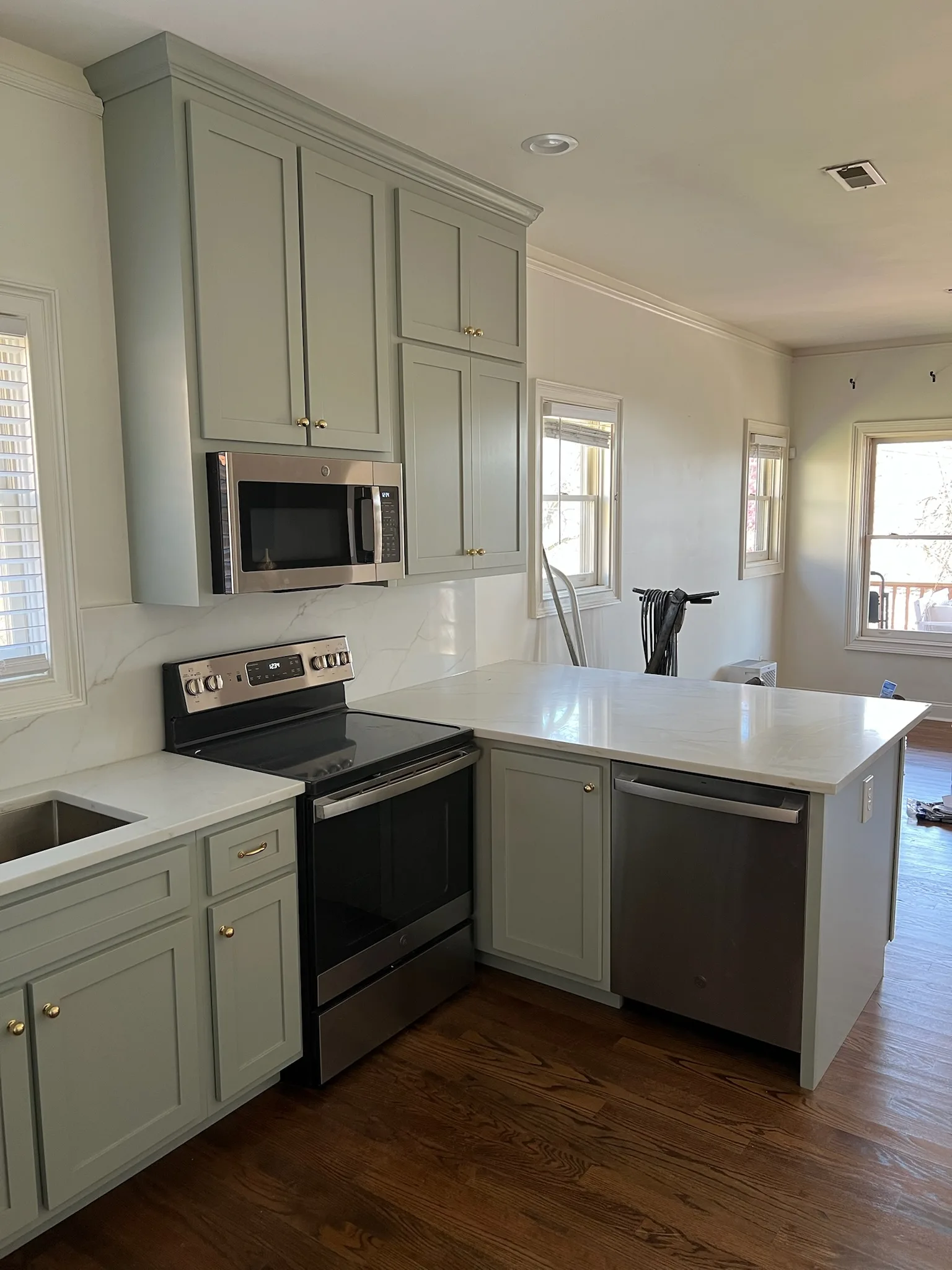 Sage green kitchen range wall with shaker cabinets and quartz backsplash by Sims Custom Woodwork.