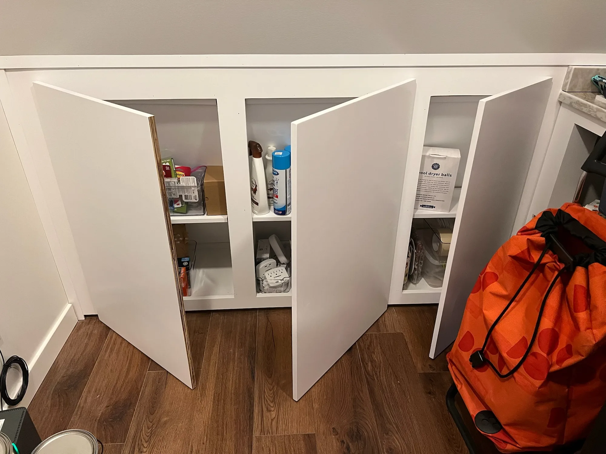 Under-stair storage cabinets with doors open showing interior shelving by Sims Custom Woodwork.
