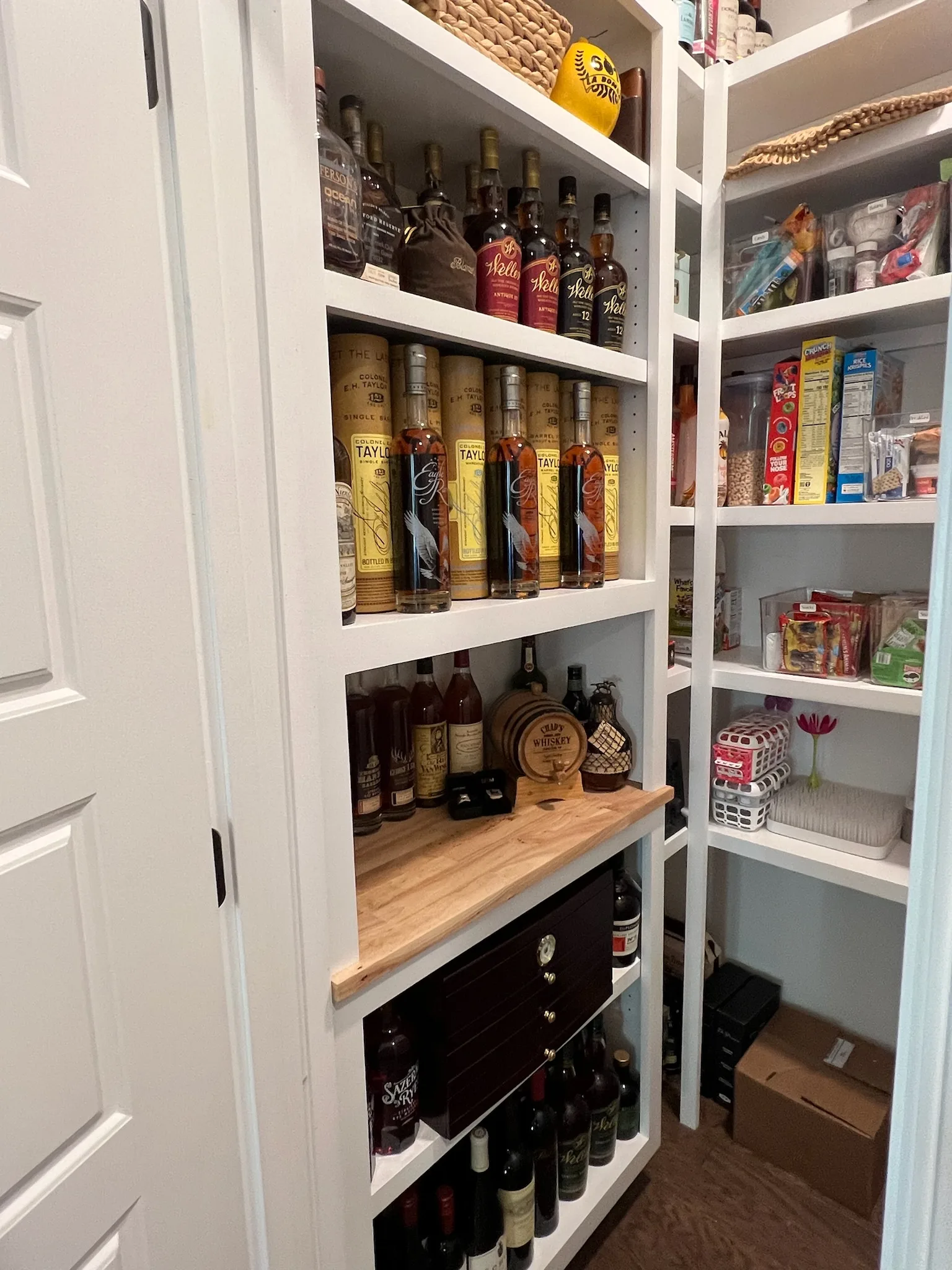 Custom walk-in pantry with white built-in shelving and wood counter accent by Sims Custom Woodwork.