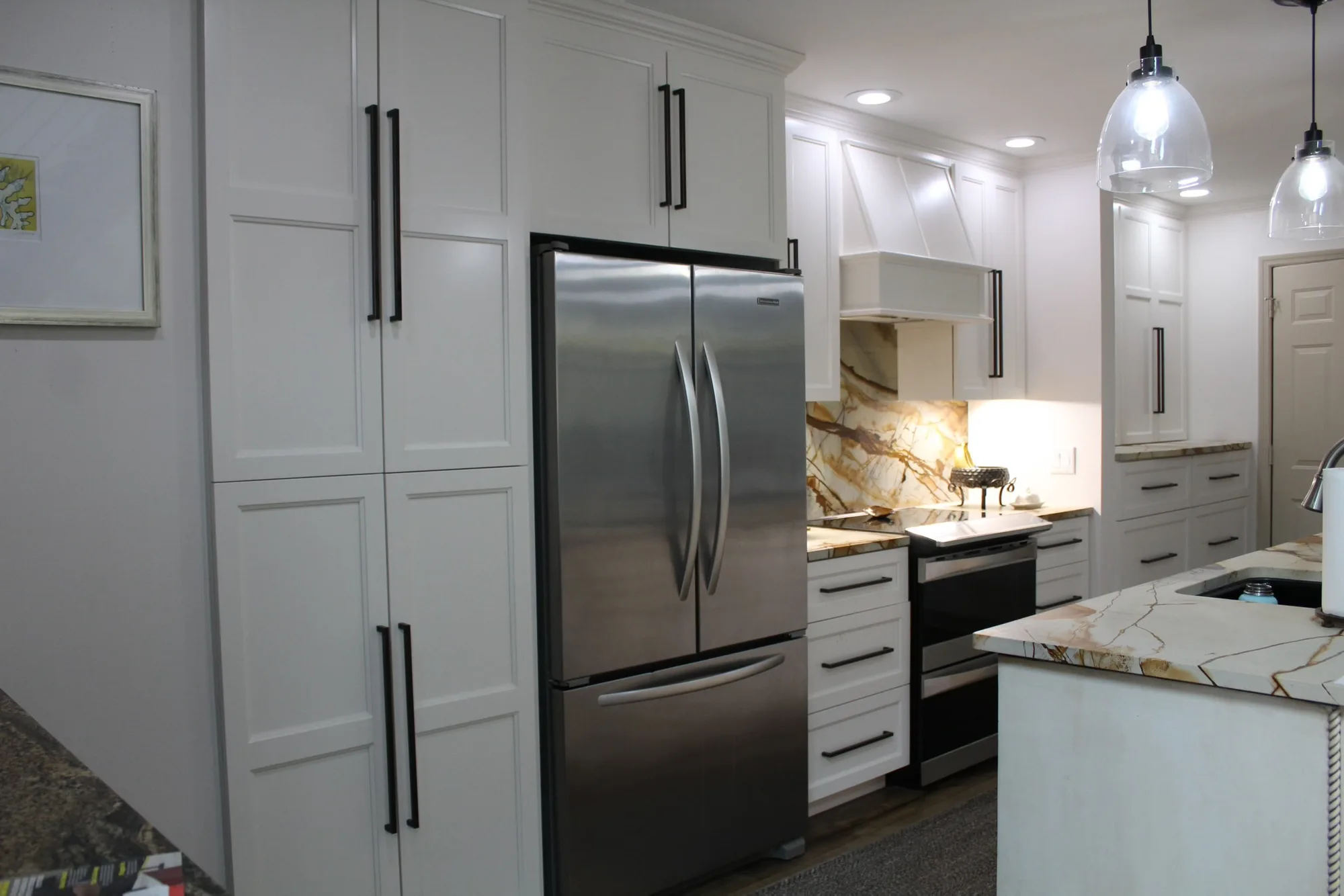 White shaker kitchen with exotic marble backsplash and floor-to-ceiling pantry cabinets by Sims Custom Woodwork.
