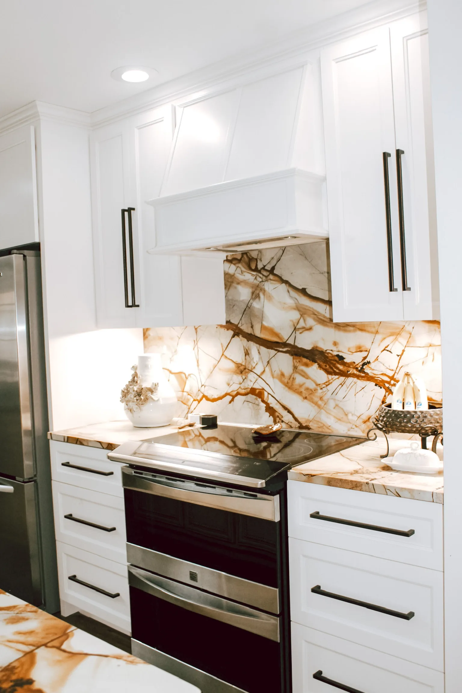 White shaker kitchen range wall with exotic marble slab backsplash and custom hood by Sims Custom Woodwork.