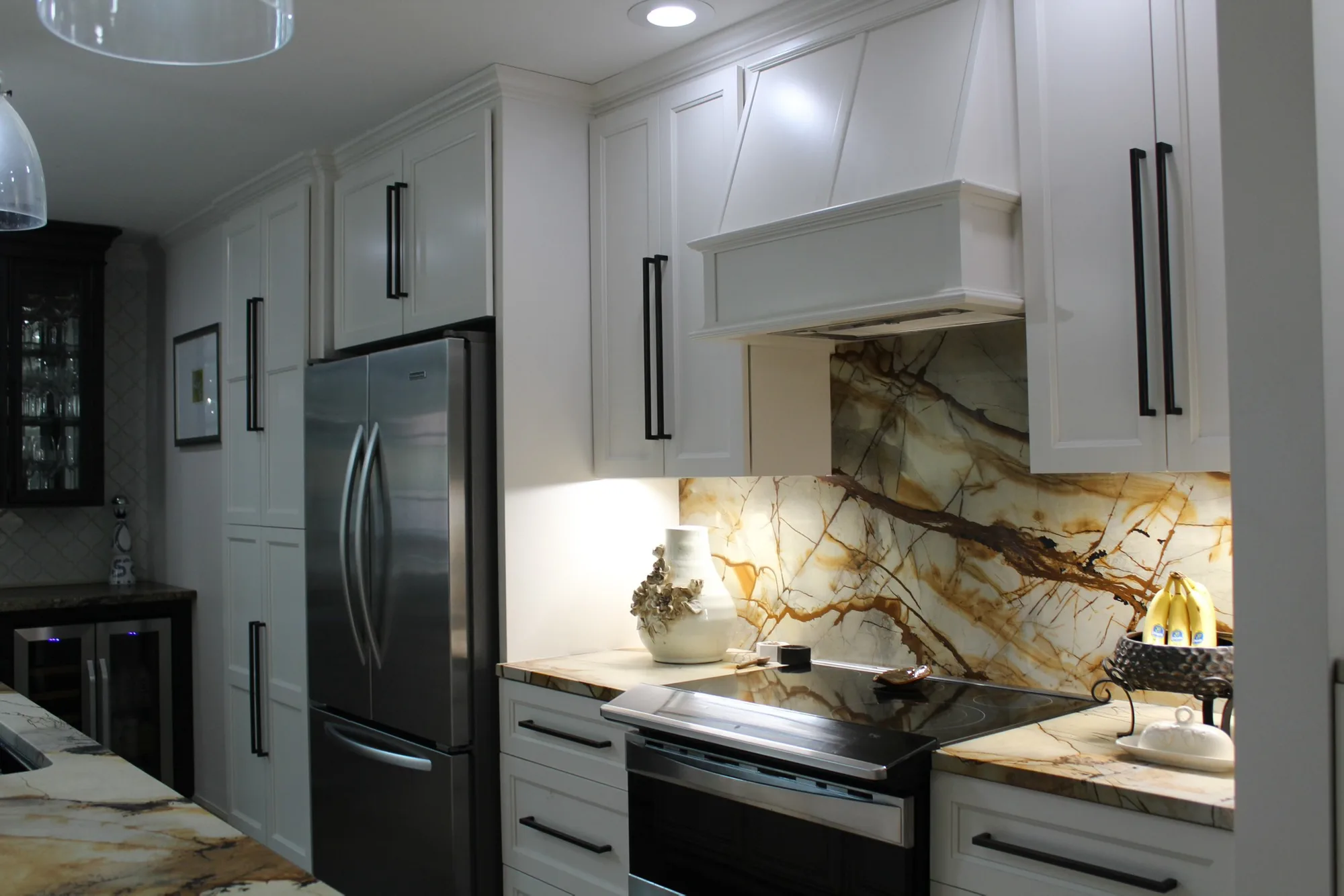 Wide-angle view of white shaker kitchen with exotic marble slab and custom hood by Sims Custom Woodwork.