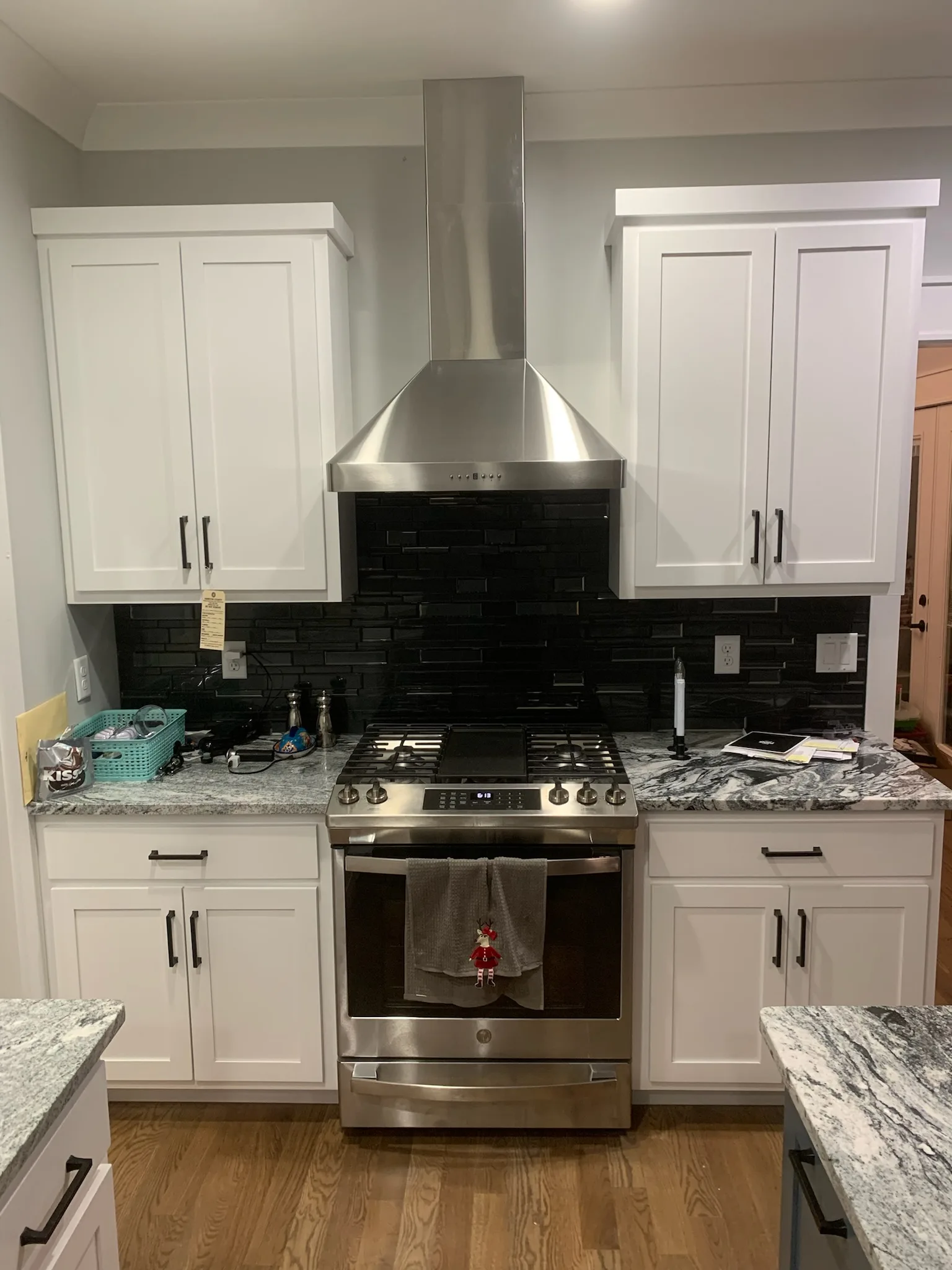 White shaker kitchen range wall with black tile backsplash and stainless hood by Sims Custom Woodwork.